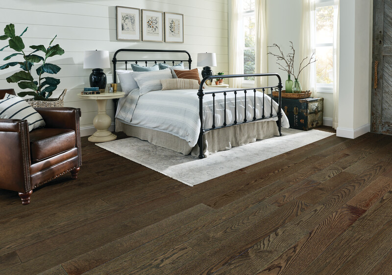 Closeup of a bed with white comforter and dark hardwood floors