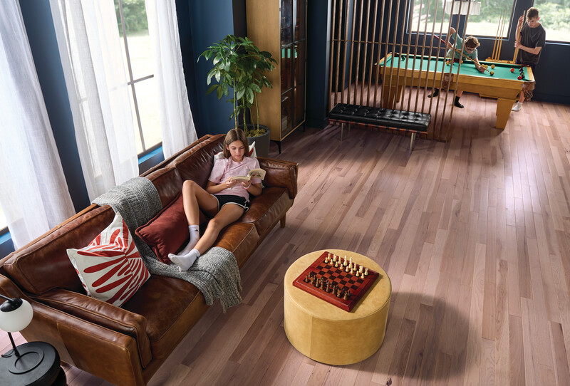 Family room with hardwood flooring and a teenager reading on a couch with a pool room in the back of the room